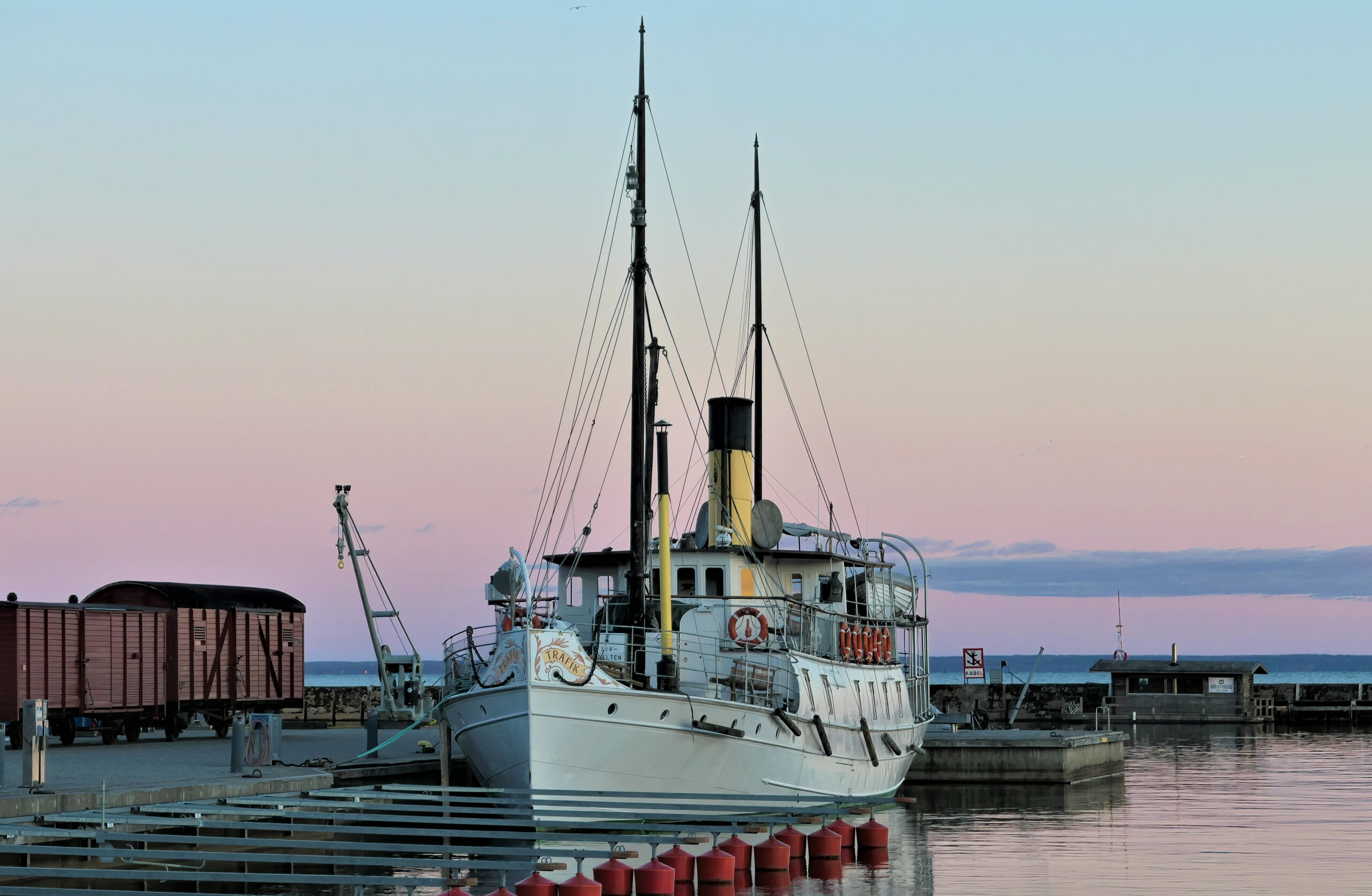Vacker skymningsbild på ångfartyget Trafik i Hjo mot en lilablå himmel och spegelblank sjö.